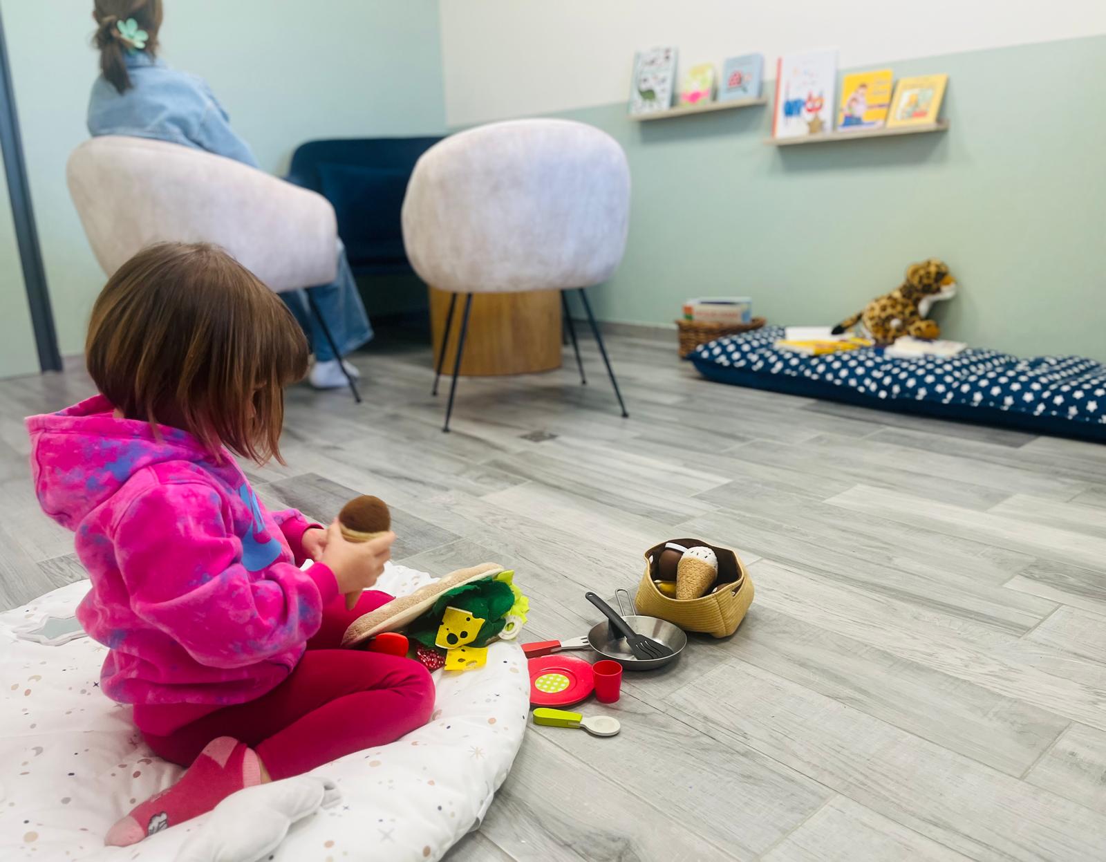 Découvrez le local chaleureux où je vous accueille. Local d’accueil chaleureux avec une enfant qui joue et une adulte de dos – illustration d’un espace d’écoute pour les familles.